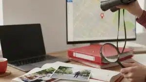 שולחן עבודה של חוקר פרטי עם משקפת, זכוכית מגדלת, תצלומים, מפה ותיקים אדומים